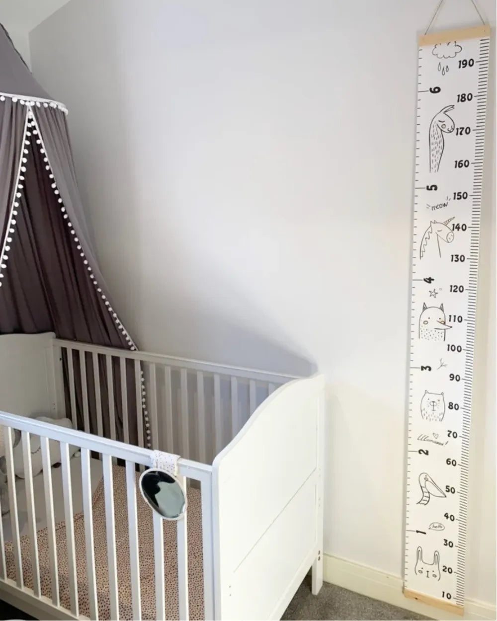 a white crib next to a white wall with a large ruler on it